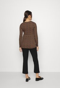 Top de manga longa em preto com padrão floral apresentando flores laranja e amarelas; combinado com calças pretas ankle e calçado preto.