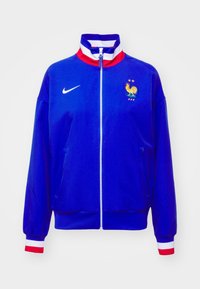 Blauwe sportjas met ritssluiting, met een boord en manchetten in rood, wit en blauw gestreept, Nike-logo en het embleem van het Franse voetbalteam met twee sterren.