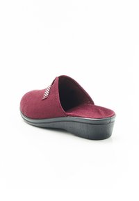 Pantofola bordeaux con tomaia in camoscio, apertura sul retro, suola in gomma nera testurizzata e imbottitura minima. Presenta un piccolo dettaglio decorativo.
