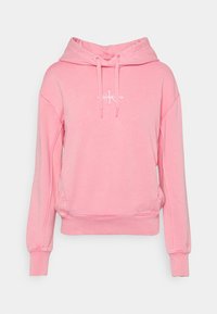 Ljusrosa hoodie i mjukt material. Har en framficka, dragsko i huvan och en diskret logotyp på bröstet.