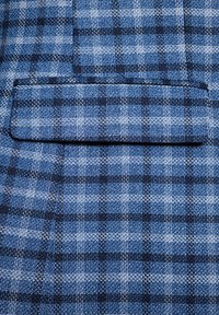 Niebieska tkanina w kratę z mieszanką jasnoniebieskich i ciemnoniebieskich tonów, z małą kieszonką. Wzór składa się z tkanych kratek o teksturowanym wykończeniu.