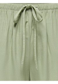 Lichtgroene broek met trekkoord en elastische tailleband, met een verticaal gestructureerd stofpatroon, vastgebonden in een eenvoudige strik aan de voorkant.