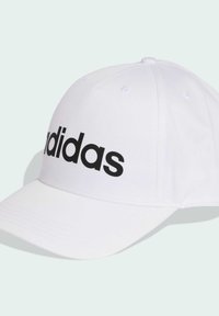 Gorra de béisbol blanca con visera curvada, que presenta un gran logo negro de "adidas" en el frente. Hecha de tela con detalles visibles de costura.