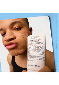 Kiehl's Ultra Facial Cleanser, 150ml, hvit tube med blå og svart tekst, med en flip-top lokk. Modell som viser produktet i nærbilde.