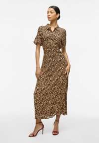 Robe maxi en imprimé léopard avec des manches courtes, un col, et des boutons sur le devant, associée à des talons hauts à lanières bordeaux.