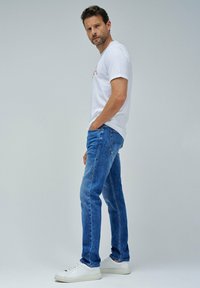 Hvid T-shirt til mænd med rødt grafisk design, parret med blå denimjeans. Jeansene har en lige pasform og er suppleret med hvide sneakers.