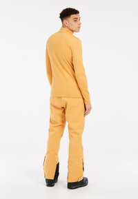 Žltý dlhý rukáv vrchný diel a zodpovedajúce nohavice vyrobené z hladkej, elastickej látky. Nohavice majú zipsy pri členkoch; celý úbor má priliehavý strih.