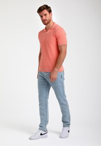 Polo tričko s krátkým rukávem, vaflové textury v korálové barvě, v kombinaci se světle modrými džíny. Obsahuje límec a žebrované manžety, doplněné bílými teniskami.