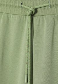 Lichtgroene joggers met een trekkoord in de taille, vervaardigd van geweven textuur en bijpassende groene uiteinden. Soepele stof met subtiele rek en zonder patronen.
