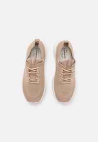 Beige stickade sneakers med en texturerad ovandel, snörstängning och vit gummisula, med en subtil logotyp på tungan.