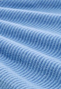 Tissu côtelé bleu clair avec une texture douce, présentant des rayures alternées de teintes variées, tombant en douces vagues.