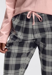 Light pink long-sleeve shirt paired with black and white plaid pajama pants, featuring an elastic waistband and drawstring.
