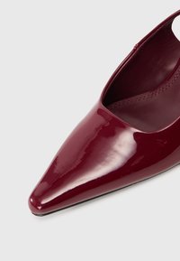 Spīdīgas bordo krāsas šauras siksniņu kurpes ar gludu ādas tekstūru un redzamām vīlēm iekšpusē.