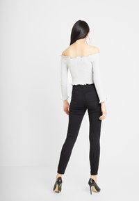 Top gris de canalé con los hombros al aire y bordes con volantes, combinado con jeans negros ajustados de talle alto y tacones de aguja negros.