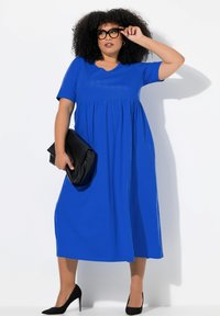 Vestido azul de manga corta con falda acampanada, escote en V y un acabado texturizado; combinado con un bolso de mano negro y tacones altos negros.