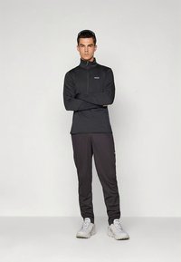 Hosszú ujjú, fekete, cipzáras sportfelső texturált mintával, fekete sportnadrággal és világosszürke tornacipőkkel párosítva.