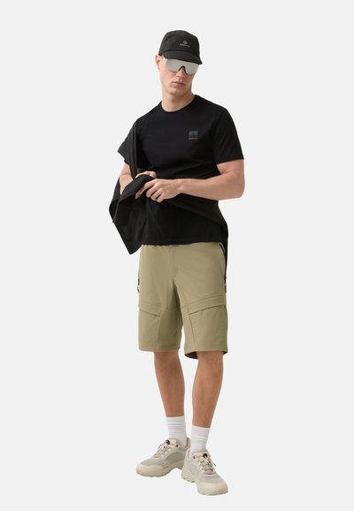 Černé tričko s malým logem, khaki cargo kraťasy s bočními kapsami, černá kšiltovka, sluneční brýle a světlé tenisky.