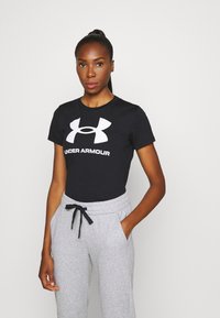 Juodas medvilninis marškinėliai su dideliu baltu "Under Armour" logotipu, derinami su pilkais sportiniais keliais su elastingu juosmeniu ir raišteliu.