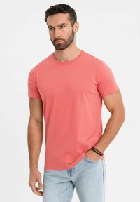 Korálová bavlněná trička s kulatým výstřihem a krátkými rukávy, spárovaná se světle modrými džíny. Jednoduchý design, měkká textura a přiléhavý střih.