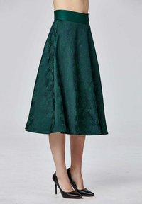 Une jupe A-line vert foncé avec un motif floral texturé et une large taille côtelée. Associée à des talons aiguilles noirs.