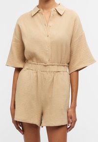 Ensemble en beige texturé comprenant une chemise à col et un short, avec une fermeture à boutons sur le devant et une taille élastique. Présente des manches courtes et une coupe décontractée.