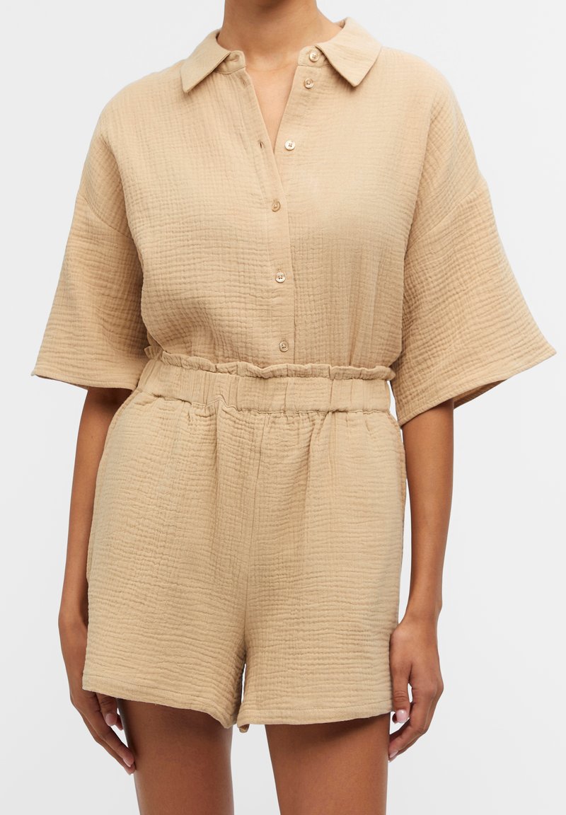 Ensemble en beige texturé comprenant une chemise à col et un short, avec une fermeture à boutons sur le devant et une taille élastique. Présente des manches courtes et une coupe décontractée.