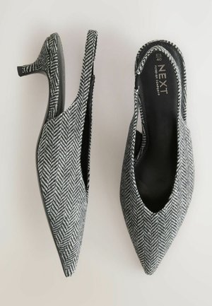 Svart och vit herringbone-mönstrad slingback-klack med spetsig tå och en smal klack. Insidan har en slät svart foder.