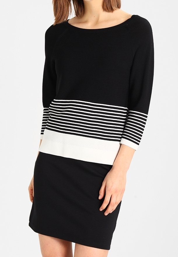 Femme portant un haut noir avec des rayures horizontales blanches et noires sur les manches basses et la taille, associé à une jupe noire unie.