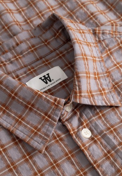 Chemise à col à boutons avec motif à carreaux orange et blanc, étiquette en tissu à l'intérieur du col portant l'inscription « Double V by Wood Wood ».