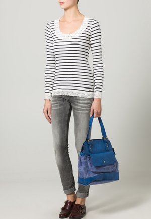 Maglia a maniche lunghe a righe con bordo in pizzo, abbinata a jeans grigi e una grande borsa azzurra con patta e doppi manici.
