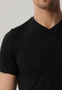 Czarna koszulka z krótkim rękawem w serek wykonana z gładkiego materiału, z dopasowanym krojem, który układa się na torsie, bez widocznych wzorów ani dodatków.