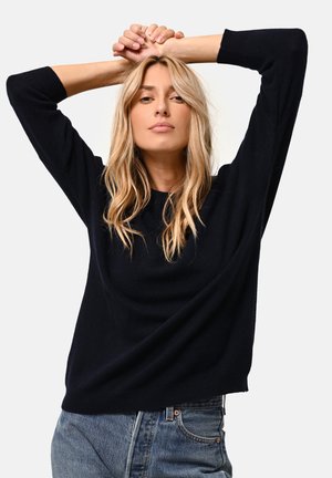 Pull bleu marine ample avec des manches trois quarts, un col rond et une texture douce, associé à un jean taille haute bleu clair.
