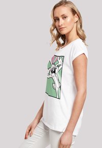 Hvit bomull t-skjorte med et trykk av Bugs Bunny på grønn bakgrunn. Korte ermer, avslappet passform, glatt tekstur.