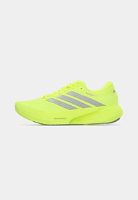 Φωτεινό κίτρινο αθλητικό παπούτσι με υφή στον επάνω μέρος, τρεις ασημένιες ρίγες στο πλάι, μαξιλαρωμένη σόλα και αεροδυναμικό, αεροδυναμικό σχέδιο.