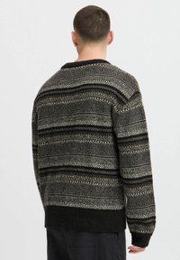 Knitted sweater in dark tones featuring a geometric pattern with stripes in black, gray, and cream. Relaxed fit; side slits at the hem.