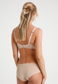 Sutiã nu com alças ajustáveis e fecho de gancho, combinado com um brief sem costuras correspondente. Tecido suave com um brilho subtil, projetado para conforto.