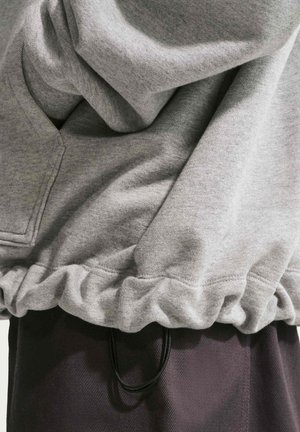 Gros plan sur l'ourlet d'un sweat-shirt gris avec un bandeau élastique sur un pantalon foncé, montrant la texture du tissu et les détails des coutures.