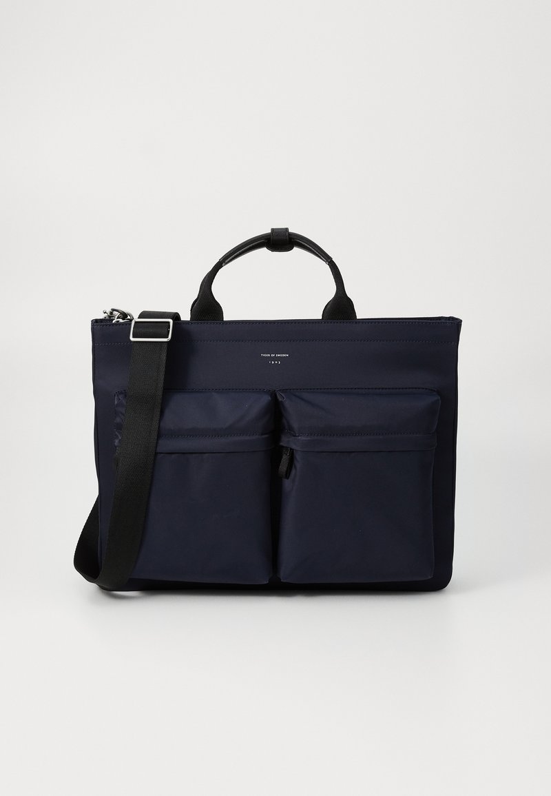 Navyblå nylon taske med to frontlommer, lynlåslukning og korte håndtag med en aftagelig skulderrem. Glat tekstur.