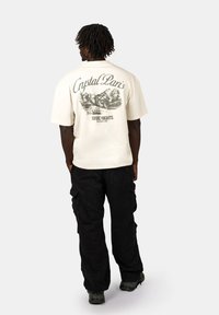 Cream-colored graphic t-shirt featuring a mountain scene and text reading "Crystal Paris Nordic Nights." Pairing with black cargo pants.