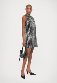 Μαύρο και άσπρο φόρεμα σε σχέδιο ψηφίδας με στρας, χωρίς μανίκια, συνδυασμένο με μια μικρή μαύρη τσάντα με χάντρες και μαύρες ψηλές γόβες.