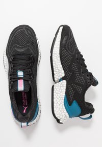 Baskets de course noires en tricot avec des semelles texturées blanches, des accents teal et des détails de marque roses, montrées de dessus et de côté sur un fond blanc.