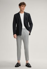 Czarna dwurzędowa marynarka z wyłogami, noszona na białym t-shircie. Szare dopasowane spodnie i czarne skórzane mokasyny dopełniają zestaw.