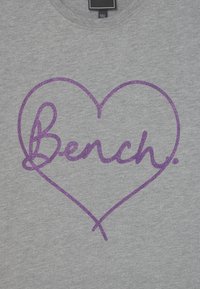 Szary t-shirt z dużym logo w kształcie serca pokrytym fioletowym brokatem, z napisem "Bench". Czytelny okrągły dekolt i miękka bawełniana tkanina.