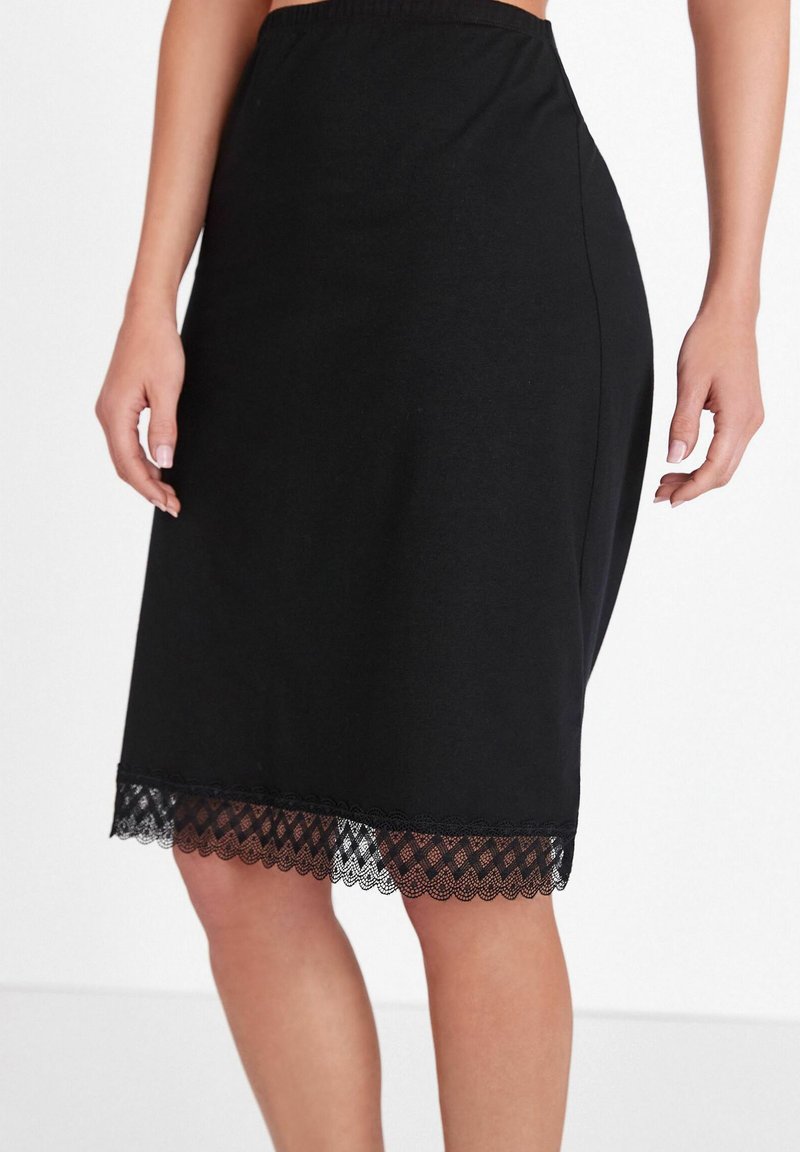 Gonna nera in cotone con vita elasticizzata, con dettaglio in pizzo all'orlo. Il design è dritto e di lunghezza al ginocchio.