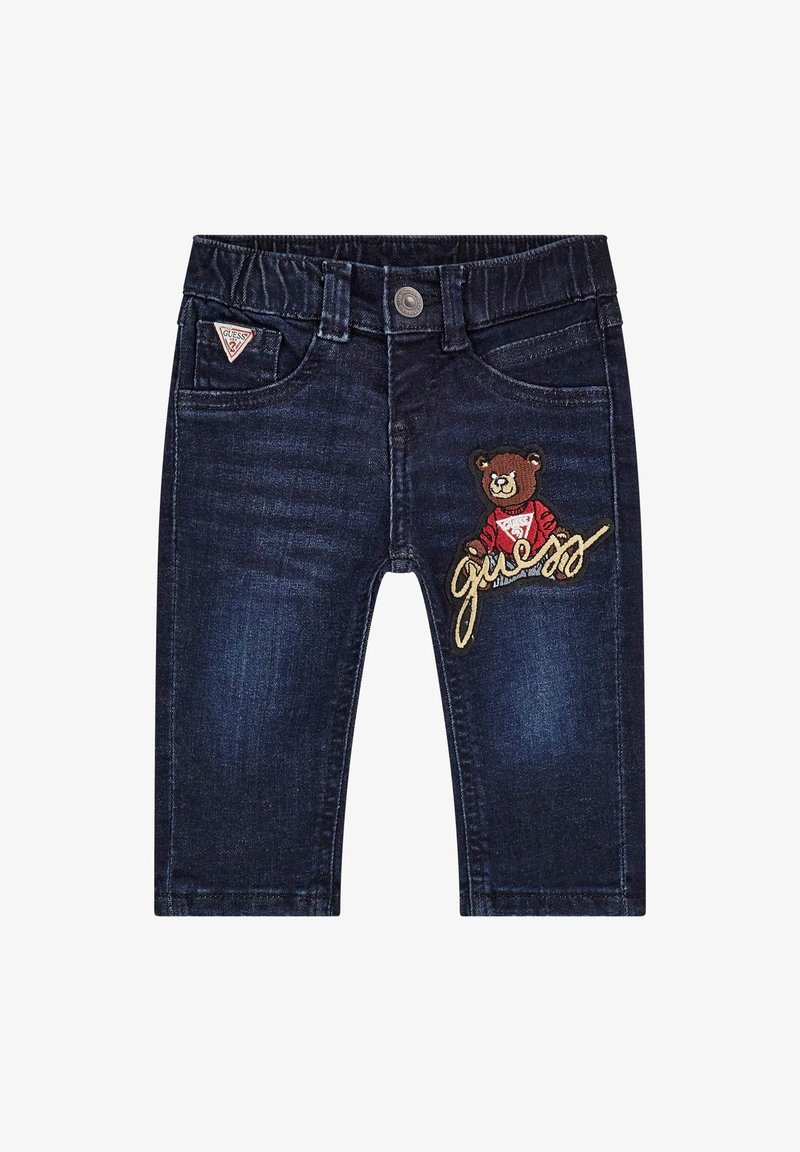 Jean bleu foncé pour tout-petit avec taille élastique, ourson brodé portant un pull rouge, et écusson logo "Guess" sur la poche avant.