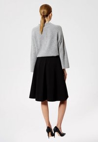 Szary sweter z dzianiny o szerokich rękawach w połączeniu z czarną, rozkloszowaną spódnicą do kolan. Modelka ma na sobie czarne buty na wysokim obcasie. Widok z tyłu.