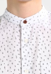 Vit skjorta med svart korshatch-mönster, bandkrage, två knappar och en bröstficka. Bomullstyg med slät yta.