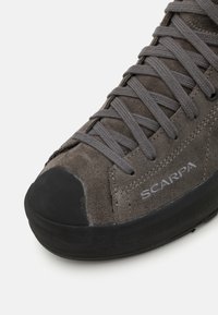 Grau Wildlederschuh zum Klettern mit einer schwarzen Gummispitze, ausgestattet mit grauen Schnürsenkeln und seitlicher Markenbeschriftung. Glatte Oberfläche mit einem robusten Design.