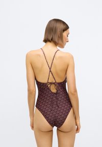 Maillot une pièce violet foncé avec un motif abstrait répétitif. Doté de bretelles fines en forme de croix dans le dos et d'une fermeture à nouer à l'arrière. Texture lisse.