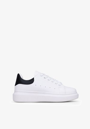 Zapatilla blanca con suela blanca gruesa, acento negro en el talón, parte superior de cuero suave y seis ojales para los cordones. Perforaciones sutiles para ventilación.